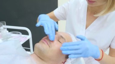 Bir adamın yüzüne yakın çekim, bir güzellik uzmanı yüzüne eldiven takarak maske takar.