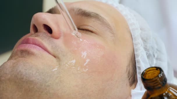 Gros plan d'un visage d'homme, sur lequel un esthéticien applique un masque sur son visage avec ses mains dans des gants — Video