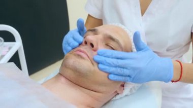 Bir adamın yüzüne yakın çekim, bir güzellik uzmanı yüzüne eldiven takarak maske takar.