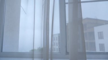 Yağmurlu bir günde penceredeki şeffaf perdeleri oynatmak