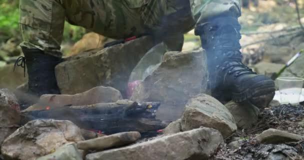 Крупным планом мужских ног в сапогах на лодыжках у огня, зажаренного на камнях — стоковое видео