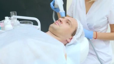 Güzellik uzmanının resepsiyonunda bir adamın yüzüne yakın çekim. Donanım kozmetoloji prosedürü ultrasonik termokaldırma uygulanıyor.