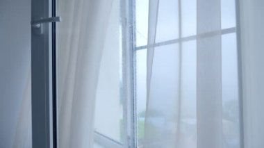 Yağmurlu bir günde penceredeki şeffaf perdeleri oynatmak