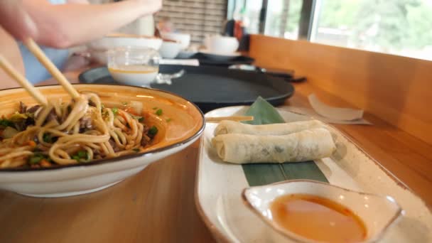 Крупный план блюд восточной кухни. люди едят азиатскую еду в кафе — стоковое видео