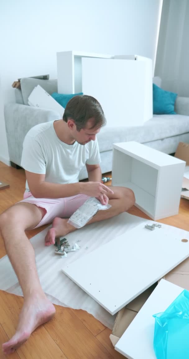 Mejoras para el hogar. un hombre ensambla muebles en un apartamento, verticalmente — Vídeos de Stock