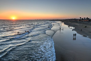 Pasifik Okyanusunda dalgalar ve günbatımında sahil manzarası, Newport Beach, California.