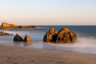 Gün batımında kayaların oluşumlarına çarpan dalgaların çarpıcı uzun süreli görüntüsü Sequit Point, Leo Carrillo State Beach, Malibu, California