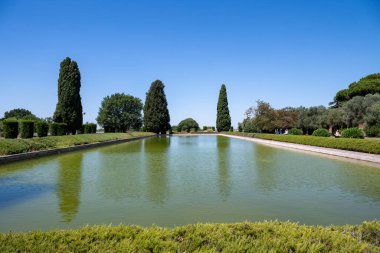 Pecile 'in Villa Adriana, Tivoli' deki büyük yansıtma havuzu. Selvi ağaçları ve gür yeşilliklerle çevrili bu dingin alan, parlak ve berrak bir gökyüzü altında Roma mimari zarafetini yansıtıyor..