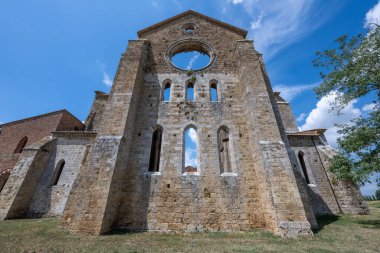 13. yüzyıldan kalma yıkık dökük San Galgano Manastırı 'nın Gotik taş cephesi Chiusdino yakınlarında aydınlık bir yaz gökyüzünün altında.