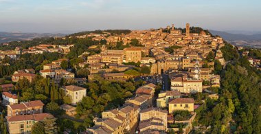 Günbatımında Toskana kırsalının üzerinde taş duvarlar, terasotta çatıları ve kuleleri gösteren ortaçağ Volterra tepelerinin hava manzarası..