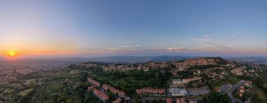 Günbatımında Volterra Tepesi 'nin insansız hava aracı panoraması, Toskana kırsalına bakan, terasotta çatıları, dolambaçlı yollar, zeytinlikler, yaz sisi.