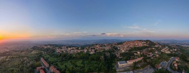 Ortaçağ Volterra Tepesi 'nin günbatımında yüksek hava manzarası. Etrafı Toskana kırsalıyla çevrili ve kırmızı kiremitli çatıları olan teraslı binalar..