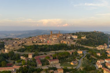 Aerial view of medieval Volterra, historic Etruscan hill town in Tuscany, with terracotta rooftops, fortress walls and surrounding countryside at dusk.