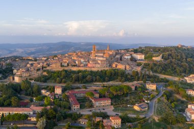 Aerial view of medieval Volterra hilltop center in Tuscany, showing stone buildings, defensive layout and surrounding rural landscape at sunset.