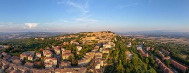 Tepesindeki ortaçağ Volterra 'sının hava manzarası taş binaları, terracotta çatılarını ve günbatımında Toskana kırsalının çevresini gösteriyor..