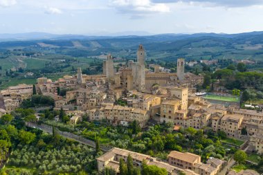 Aerial view of San Gimignanos medieval stone towers and walls rising above Tuscan countryside, a former Via Francigena trading hub.