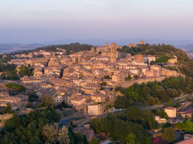 Tuscany, Volterra 'nın ortaçağ tepe kasabasının hava manzarası günbatımında kompakt taş binalar, savunma duvarları ve çevre kırsal bölgeleri gösteriyor..