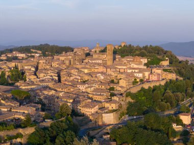 Aerial view of Volterra hilltop historic center at sunset, dense stone buildings and medieval towers rising above Tuscan countryside.