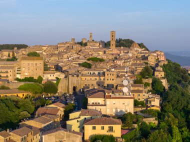 Ortaçağ Volterra 'sının günbatımındaki görüntüsü, yoğun taş evler, terasotta çatıları, tepe duvarları ve Toskana kırsalının çevresini gösteriyor..