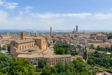 Tuğla Gotik Bazilikası Cateriniana San Domenico, Siena 'da belirgin çan kulesi, geniş manzaralar ve açık yaz gökyüzü altında sıcak terasotta renkleri bulunur.