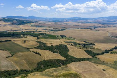 İtalya 'nın Pienza yakınlarındaki Toskana tepeleri canlı yaz renkleriyle görülebilir. Patchwork alanları ve dolambaçlı yollar, parçalı bulutlu bir gökyüzü altında bölgenin tarım mirasının altını çiziyor.