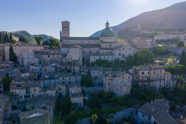 Santa Maria sopra Minerva Kilisesi manzarası, Assisi, İtalya. Antik Roma tapınağı cephesi, çan kulesi. Ortaçağ taş binalarında sıcak güneş ışığı ve yuvarlanan tepeler..