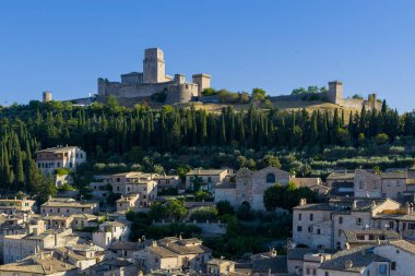 İtalya 'nın Assisi kentindeki bir ortaçağ kalesi olan Rocca Maggiore, taş mimarisi ve kasabanın hakim manzaralı bir tepenin üzerinde yer alıyor. Öğleden sonra ışığı tarihi siluetini güçlendiriyor..