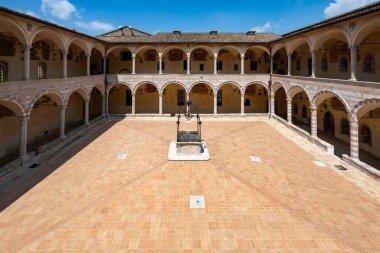 Assisi, İtalya - 17 Temmuz 2025: Assisi, İtalya 'daki Papalık Bazilikasının iç avlusu. Parlak bir yaz gökyüzünün altında taş kemerler ve fayanslı avlu.