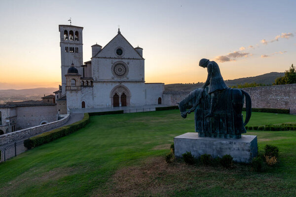 Gothic basilica in Assisi, Italy, famous for 13th-century architecture, features rose window, intricate facade, illuminated at night, site linked to Saint Francis, important pilgrimage destination.