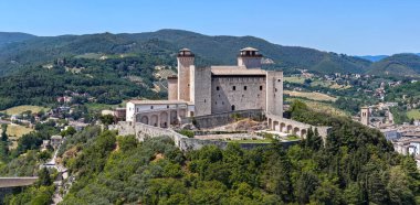 Spoletos tepesinin tepesine tünemiş Rocca Albornoziana ortaçağ askeri mimarisini sergiliyor. 14. yüzyılda inşa edilen taş duvarlar ve kuleler yemyeşil ve berrak gökyüzüne karşı çerçevelenmiştir.. 
