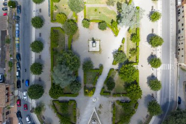 San Gimignano 'daki Piazzale Martiri di Montemaggio parkının dikey hava görüntüsü, merkez anıtı, ağaçlık yolları ve çevre sokakları gösteriyor..