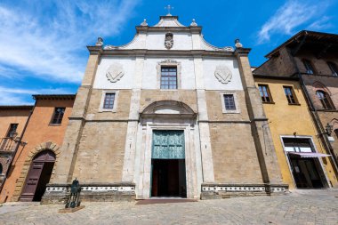 Volterra, Toskana 'daki Aziz Mikail Kilisesi' nin barok taş cephesi mavi gökyüzünün altındaki tarihi konaklar tarafından çerçevelenmiştir..