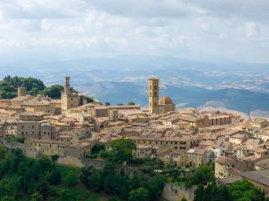 Tuscany 'deki Volterras ortaçağ siluetinin gökyüzü manzarası, taş kuleleri, terracotta çatıları ve bulutların altındaki kırsal bölgeler..