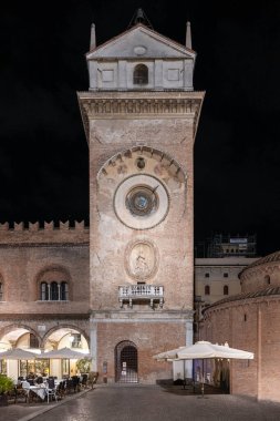Mantua, İtalya - 24 Temmuz 2025: Rönesans tuğlası Torre dellOrologio ve Piazza Erbe, Mantua 'da ortaçağ Rotonda di San Lorenzo, gece kafe teraslarının üzerinde aydınlandı.