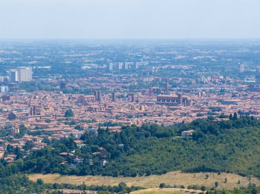 Bolonya 'nın yüksek hava manzarası ortaçağ kırmızı çatılı şehir merkezini, dağınık kuleleri ve sisli bir yaz gününde çevreleyen yeşil tepeleri gösteriyor..