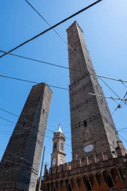 Ortaçağ Asinelli 'sinin alçak açılı görüntüsü ve Bolonya' daki eğimli Garisenda kuleleri, açık bir yaz gününde tramvay kabloları tarafından çerçevelenmiş tuğla yapı.