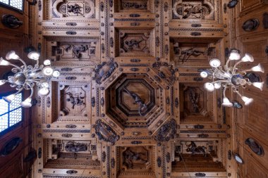 Bologna, İtalya - 23 Temmuz 2025: Rönesans ahşap kaplama tavan, Archiginnasio Bolonya Belediye Kütüphanesi 'nde oyulmuş alegorik figürler ve avizeler.