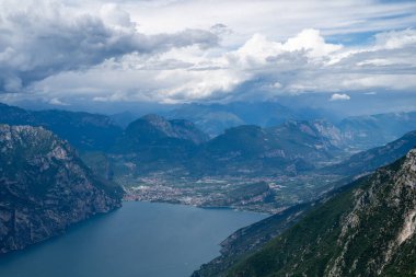 Kuzey Garda Gölü üzerinden Baldo Dağı 'nın yüksek manzarası dik kireçtaşı yamaçlarını, Malcesine kıyılarını ve fırtınalı yaz bulutlarını gösteriyor..