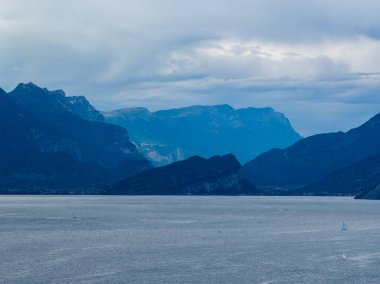 Malcesine 'den Garda Gölü' ne, bulutlu yaz gökyüzünün altındaki katmanlı Prealp tepelerine doğru kasvetli bir manzara..