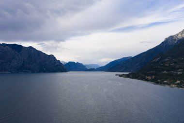 Malcesine yakınlarındaki Garda Gölü 'nün kuzey havzasında, dramatik yaz bulutları altında dik dağlık yamaçlar tarafından çerçevelenmiş hava manzarası..