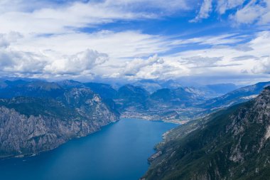 Kuzey İtalya 'daki dramatik yaz bulutları altında dik Alp yamaçlarının çerçevelediği Garda Gölü ve Riva del Garda' nın yüksek hava manzarası..