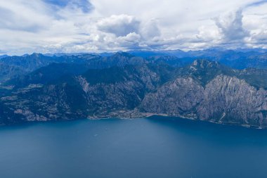 Garda Gölü 'ndeki Limon Konsolosu Garda' nın üzerinden geçen yüksek hava manzarası, yaz bulutlarının altında kıyı şeridine inen dik dağlık yamaçları gösteriyor..