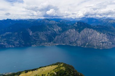 Garda Gölü 'ndeki Limone Sul Garda üzerinde yüksek hava manzarası dik Alp yamaçlarını, mavi suları ve yaz bulutlarının altında dağılmış tekneleri gösteriyor..