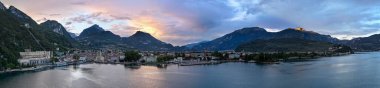 Alacakaranlıkta Garda Gölü 'ndeki Riva del Garda limanının geniş panoramik manzarası Trentino dağları ve tarihi göl binaları tarafından çerçevelenmiştir..