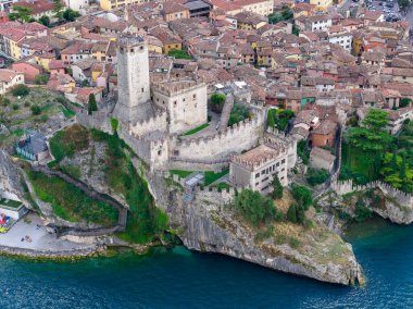 Malcesine 'deki Garda Gölü üzerindeki kayalık kayalıklarda bulunan ortaçağ Castello Scaligero kalesinin havadan görünüşü, tarihi kiremit çatılı evlerle çevrili..