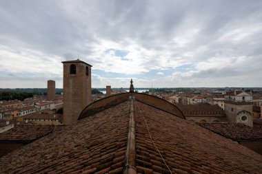 Basilica di SantAndrea 'nın terasotta çatı sırtı ortaçağ tuğla kulelerine ve Mantua' da bulutlu yaz gökyüzünün altındaki tarihi gökyüzüne bakıyor..