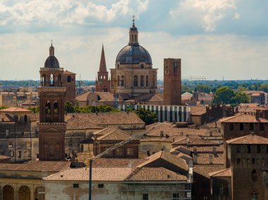 Aerial view of Mantua skyline featuring Basilica of SantAndrea dome, medieval brick towers, terracotta roofs under summer clouds.