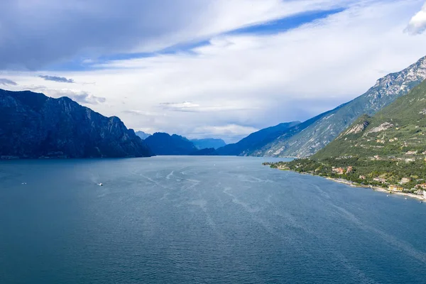 Malcesine yakınlarındaki Garda Gölü üzerindeki hava manzarası, derin mavi suyu, ormanlık dağları, uzak Trentino dağlarını ve yaz gökyüzünü gösteriyor..