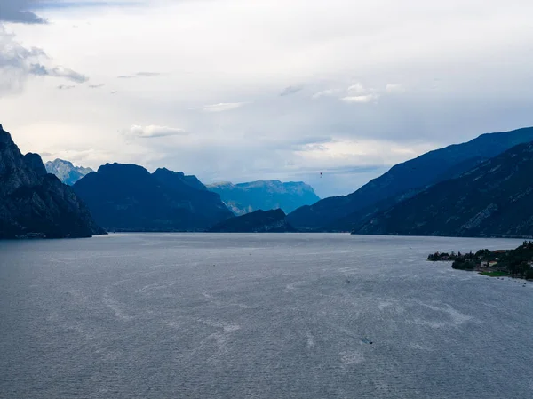 Kuzey havzası boyunca uzanan bulutlu yaz gökyüzü altında Garda Gölü 'nün dalgalı sularını çevreleyen uzak dağ sırtları..