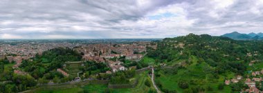 Yeşil bir vadiye bakan tepelik bir şehrin geniş hava manzarası kompakt tarihi binaları, teraslı yamaçları ve çevresindeki kırsal alanları gösteriyor..
